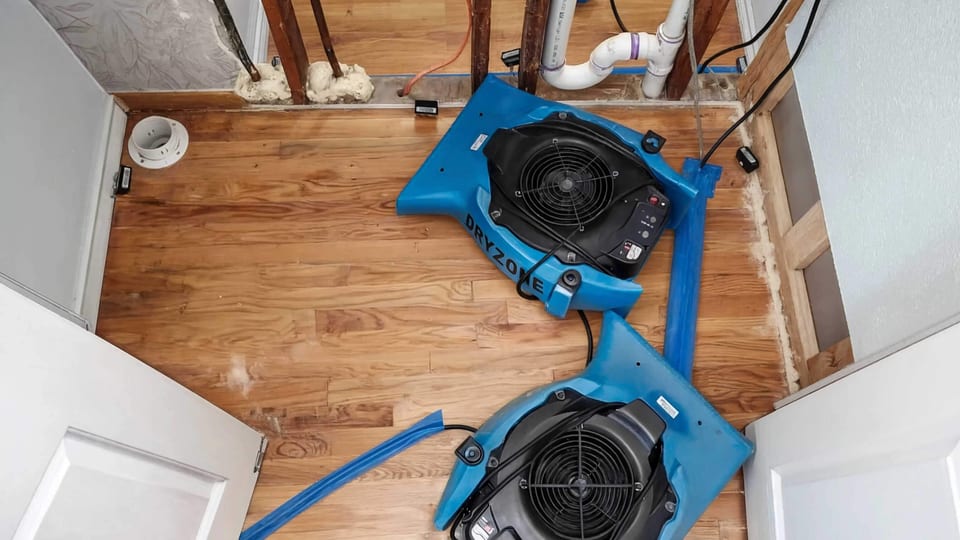 Air movers and a dehumidifier drying a water-damaged room